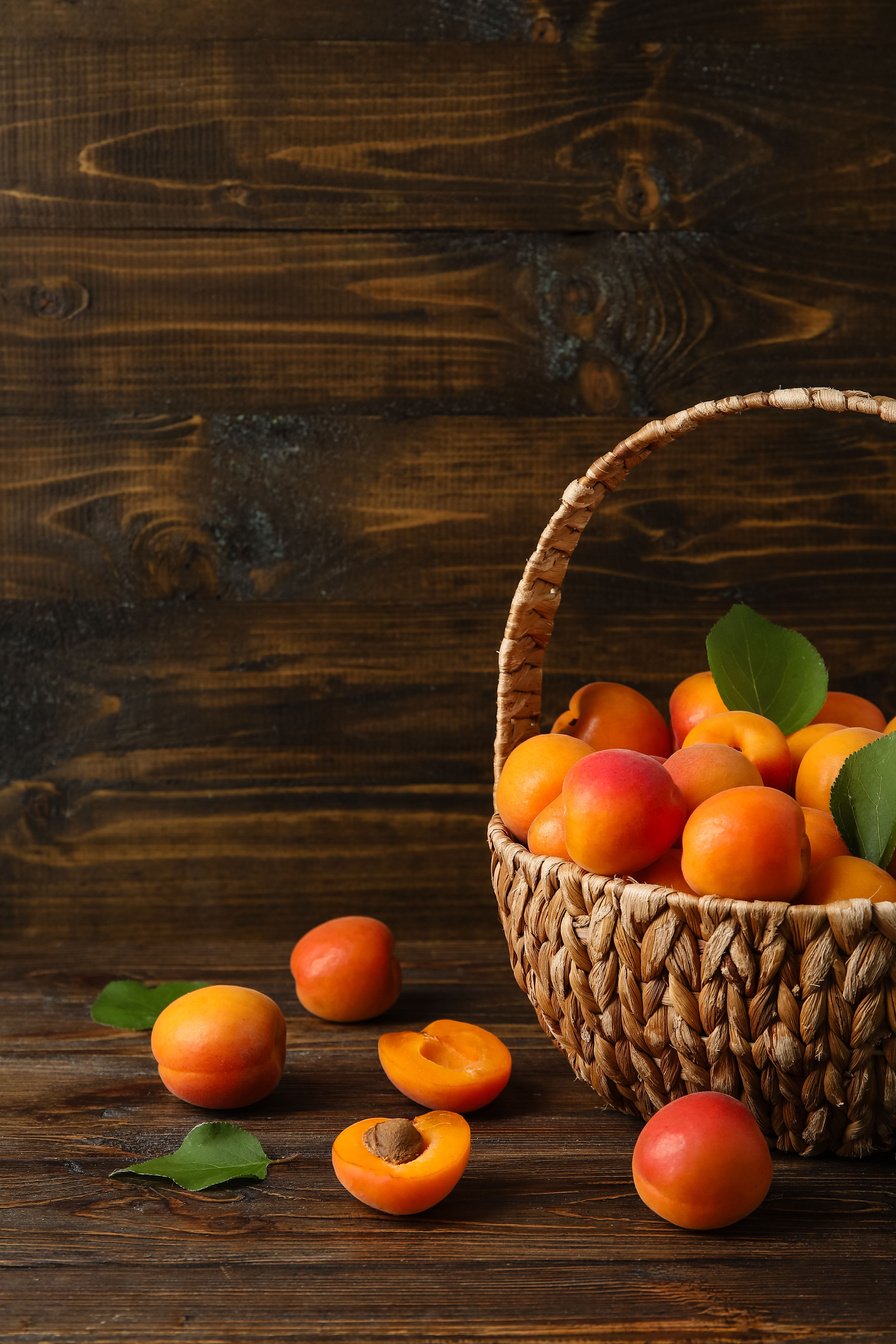 Wicker Basket with Fresh Apricots on Wooden Background